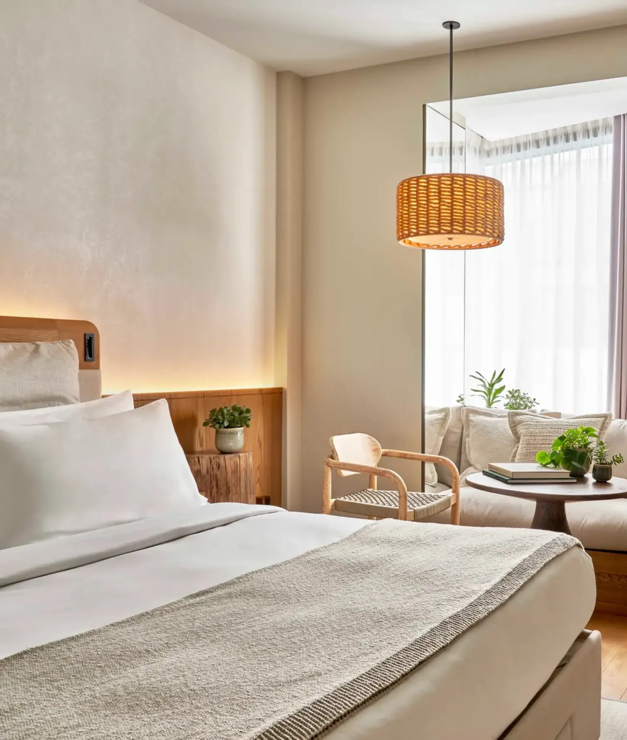 A bright King room with a rattan lamp and a seating corner by the window.