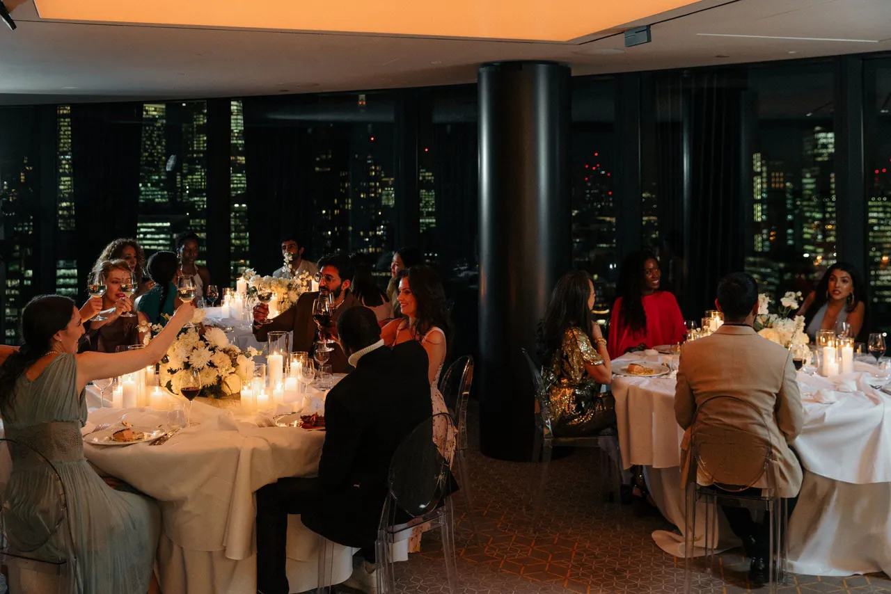 Guests dining by candlelight with the city lit up behind them.