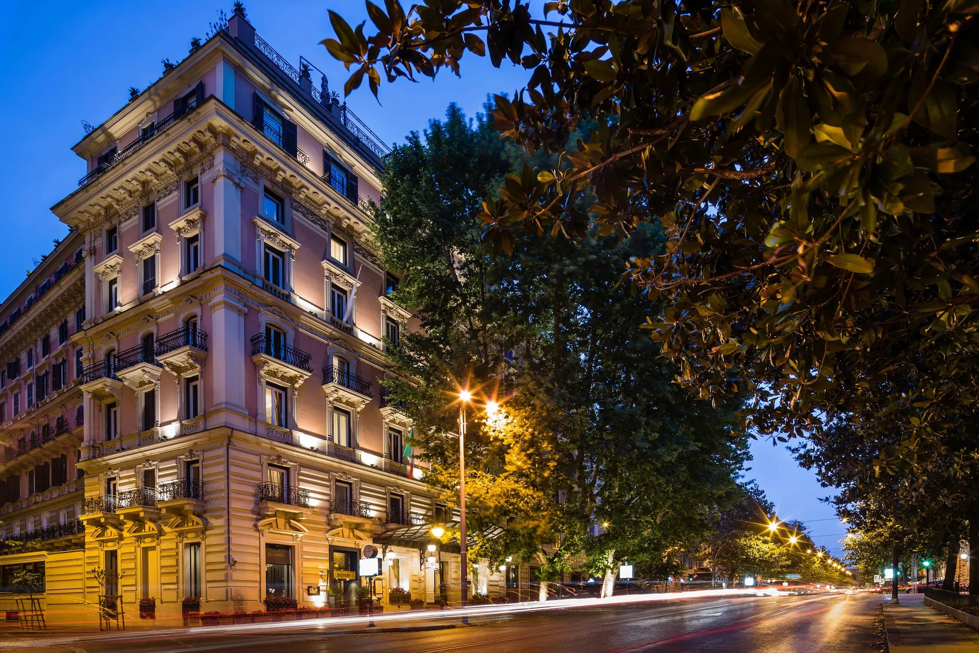The stone facade of Baglioni Hotel Regina lit up at dusk on Via Vittorio Veneto.