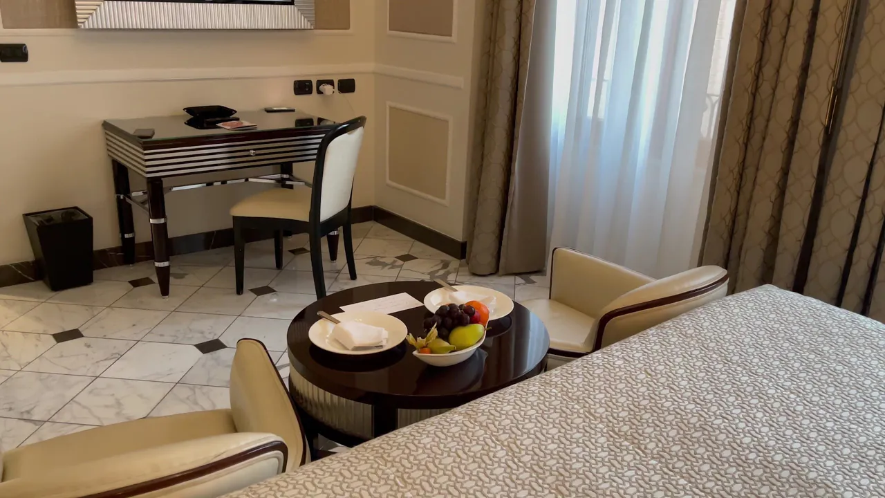 A cream guest room with a writing desk, armchairs and a fruit plate by the window.