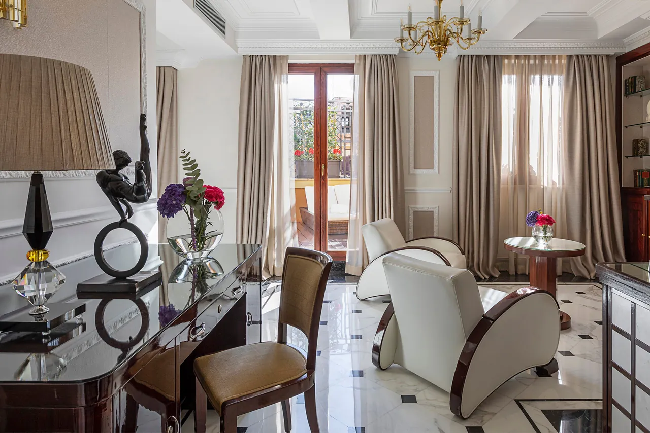 A suite living room with white armchairs, fresh flowers and doors to a terrace.