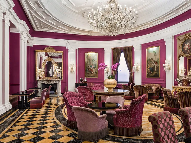 A crimson salon with a crystal chandelier, gilded paintings and a chequered marble floor.
