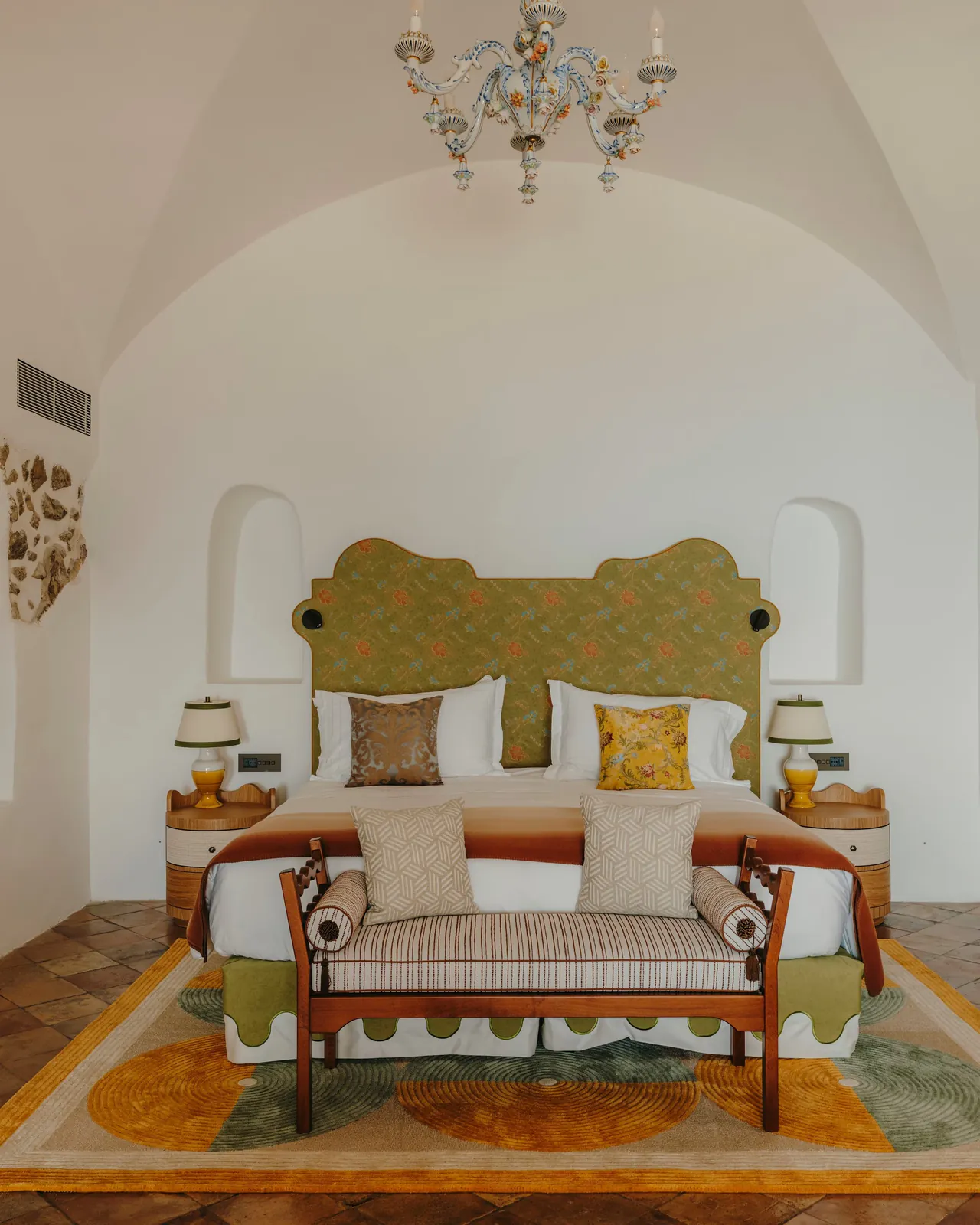A Divina Suite bedroom with stone walls, a gilded bedhead and terracotta floors.