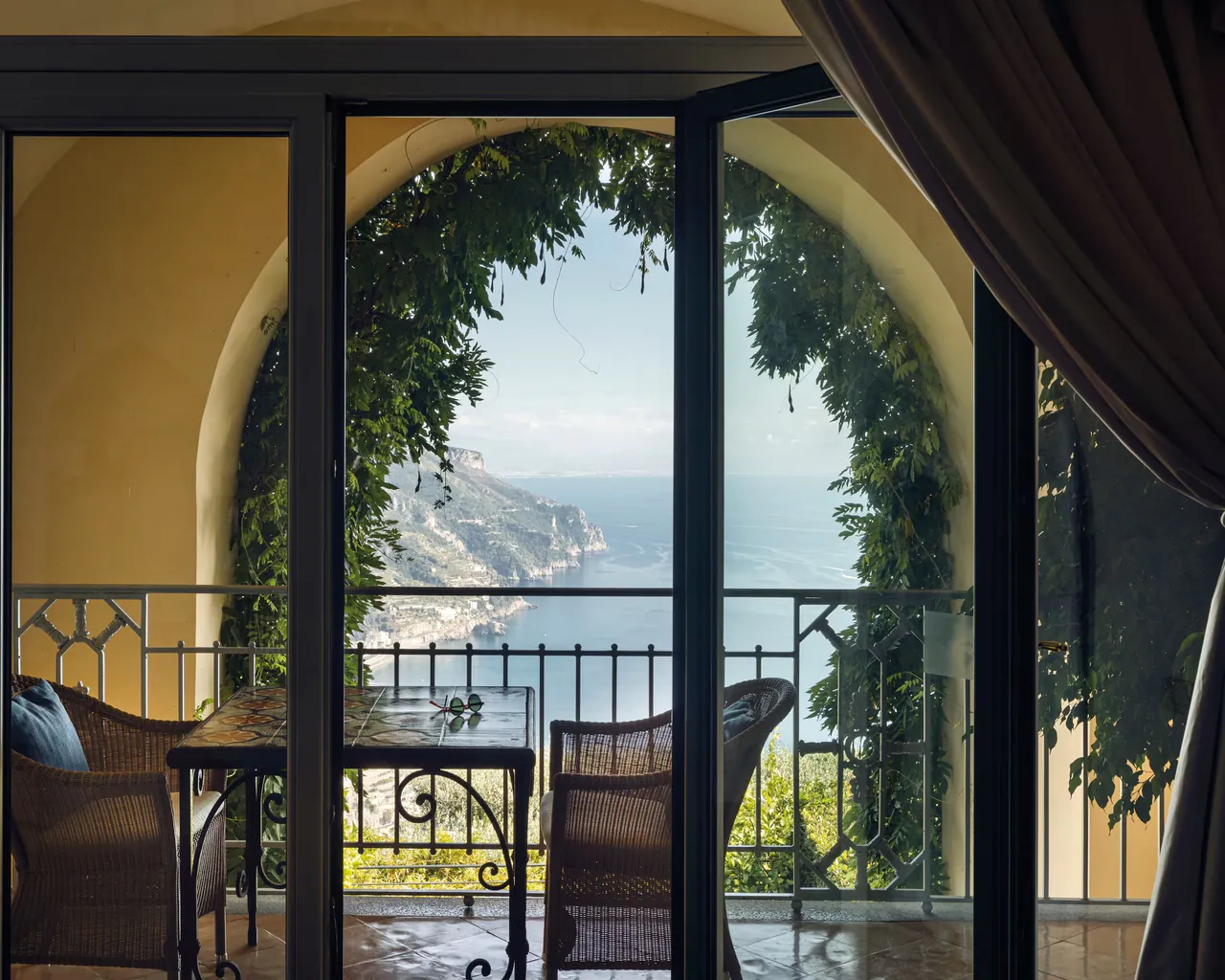 A yellow arch hung with greenery frames a balcony view down the coast.