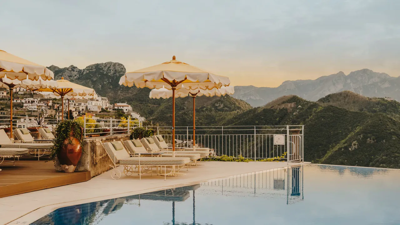 Scalloped parasols and loungers along the infinity pool, with the mountains behind.
