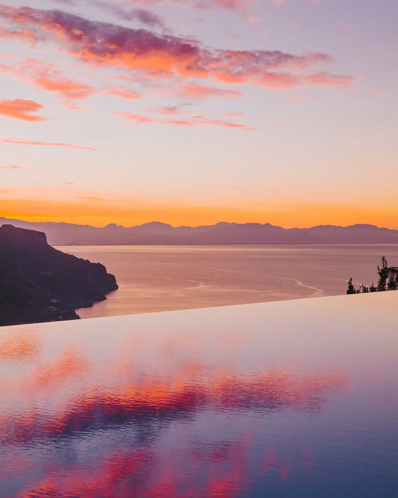 The infinity pool mirrors a pink and orange sunset over the gulf.