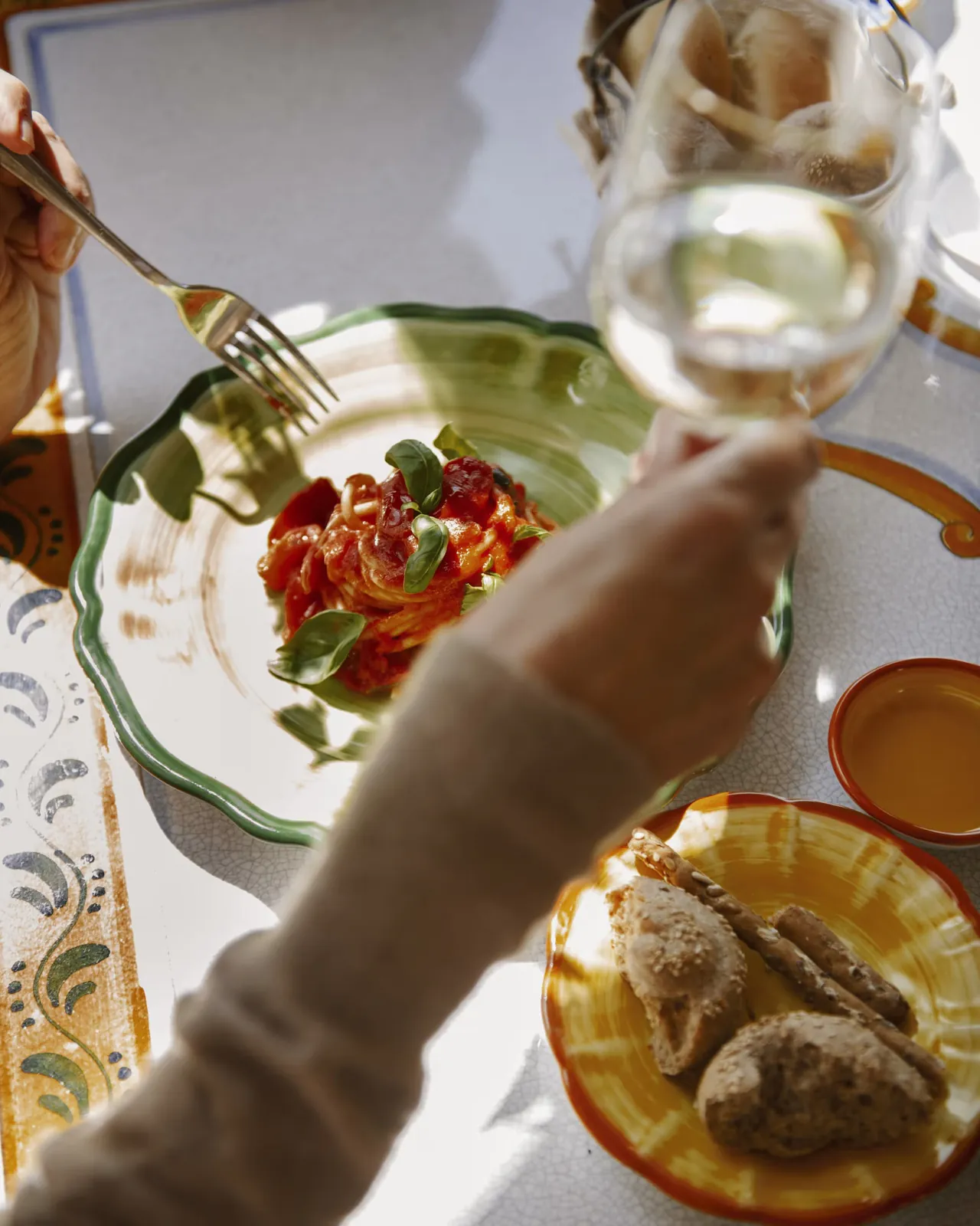 Pasta with tomatoes, bread and a glass of white wine at a lunch table.