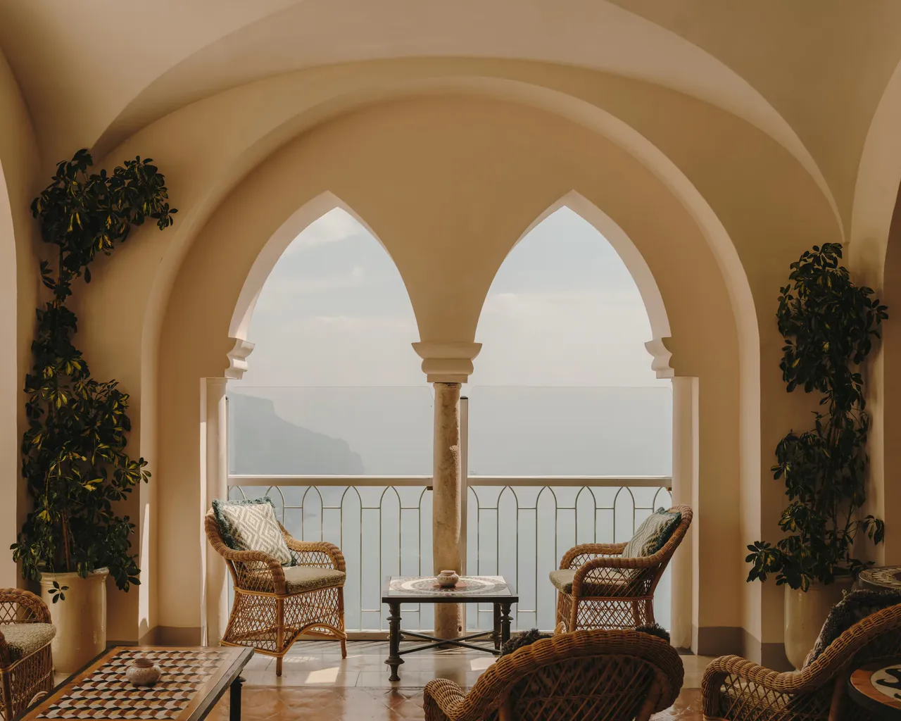 Wicker chairs in a vaulted loggia whose Gothic arches open onto the coast.