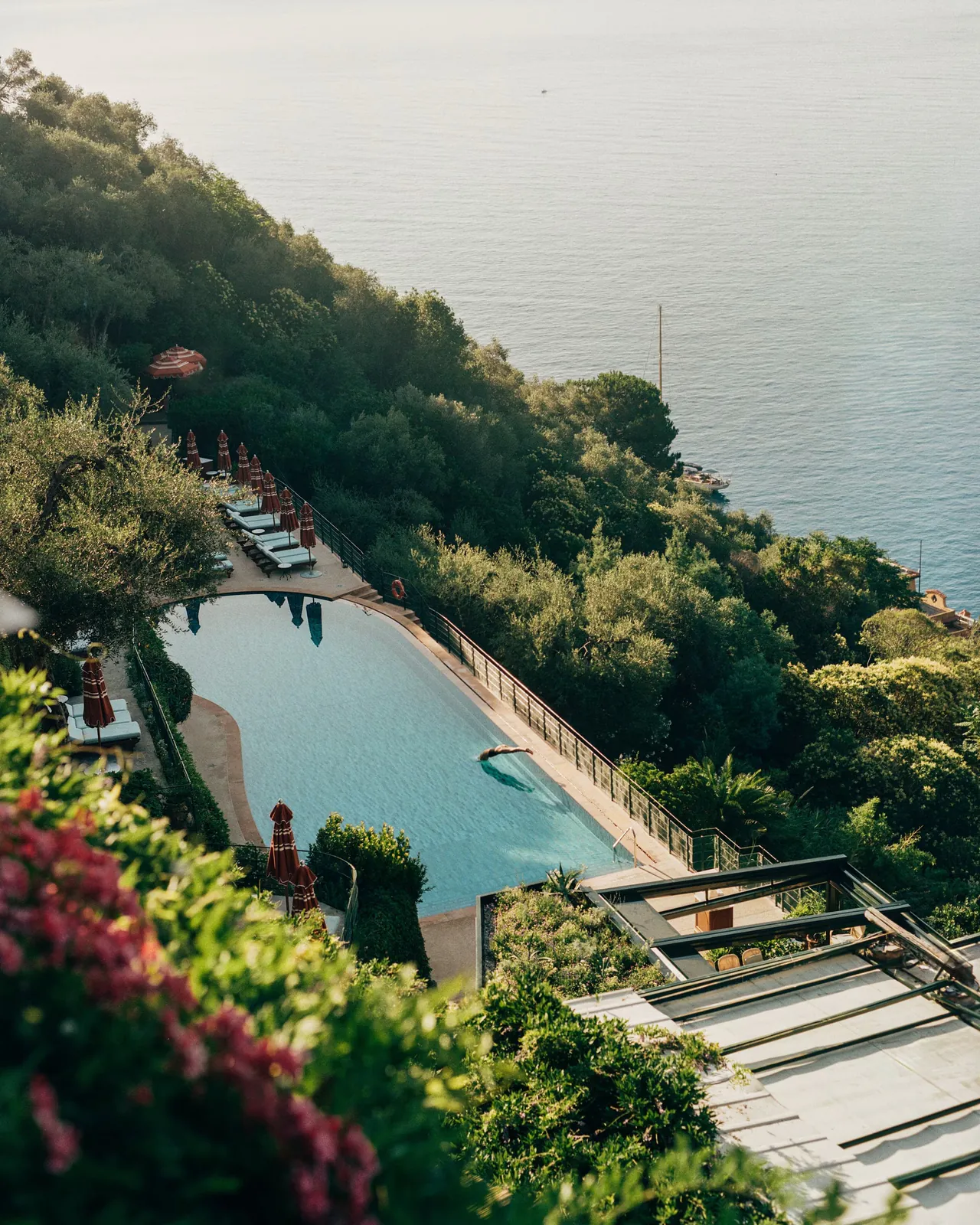 The pool on its terrace, set into the green hillside above the sea.