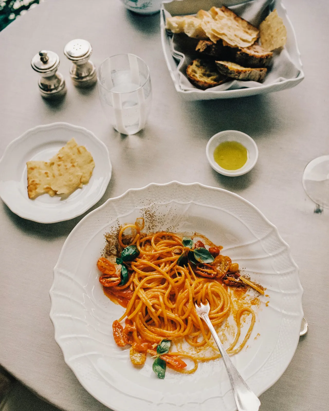 Spaghetti with tomato, bread and olive oil on a white tablecloth.
