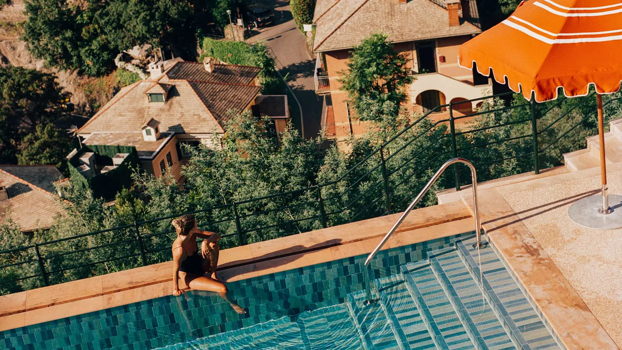 A guest at the edge of the pool, seen from above, with terracotta roofs below.