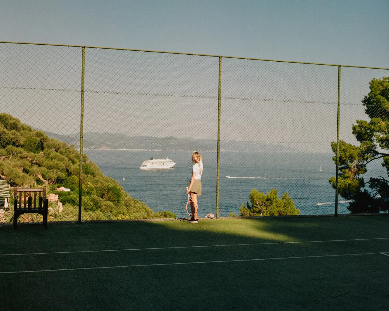 The tennis court on the hillside, with the sea and a passing ship beyond.