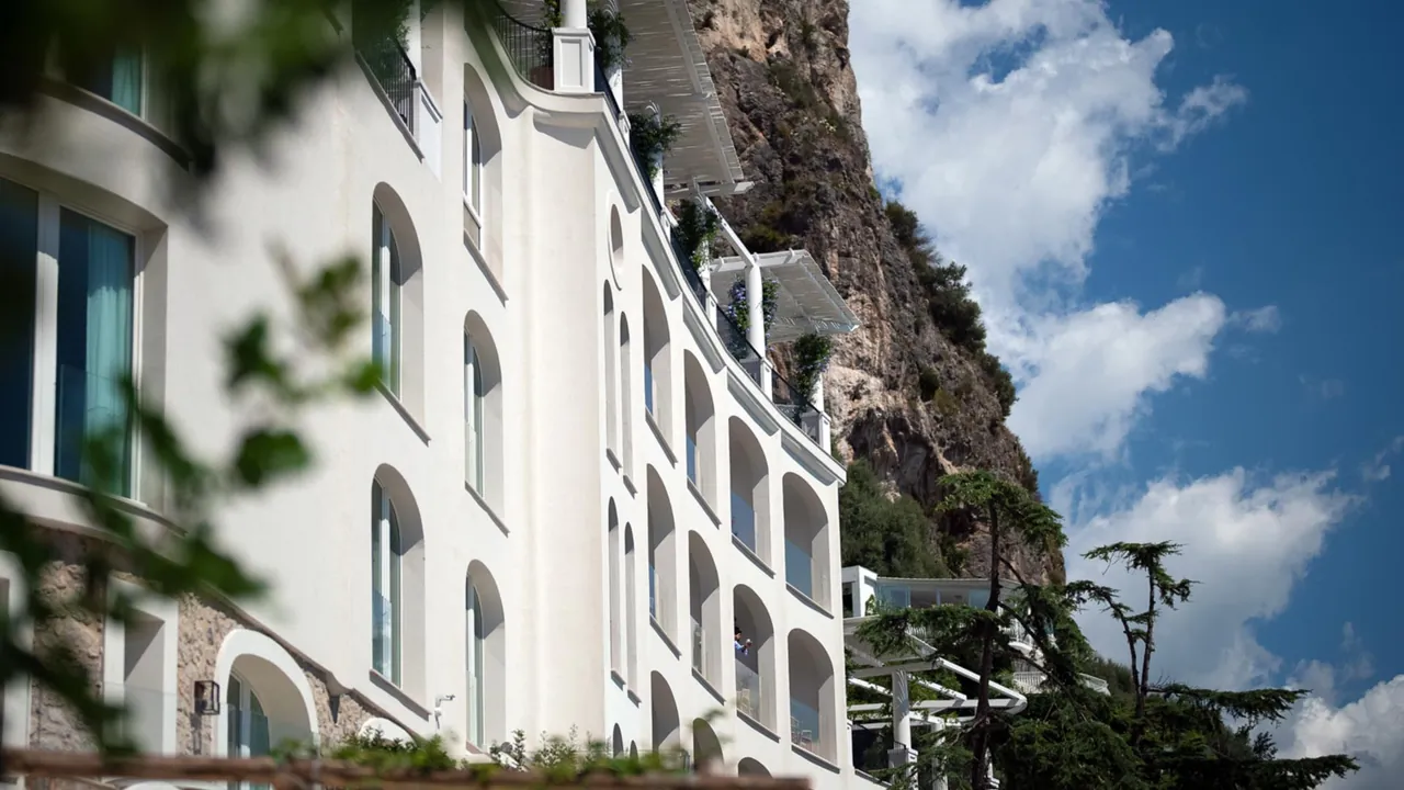 The white arched facade of the hotel against the cliff and a blue sky.