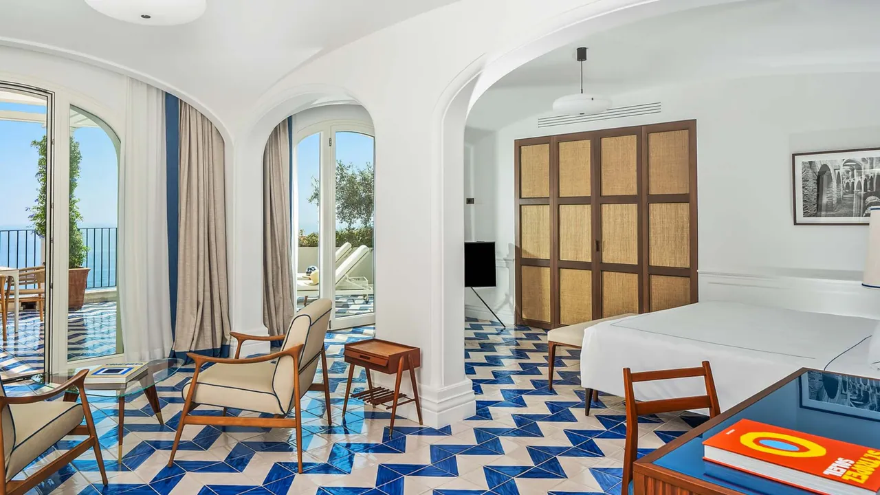 A suite with blue and white zigzag tiles, mid-century chairs and doors to a sea-view terrace.