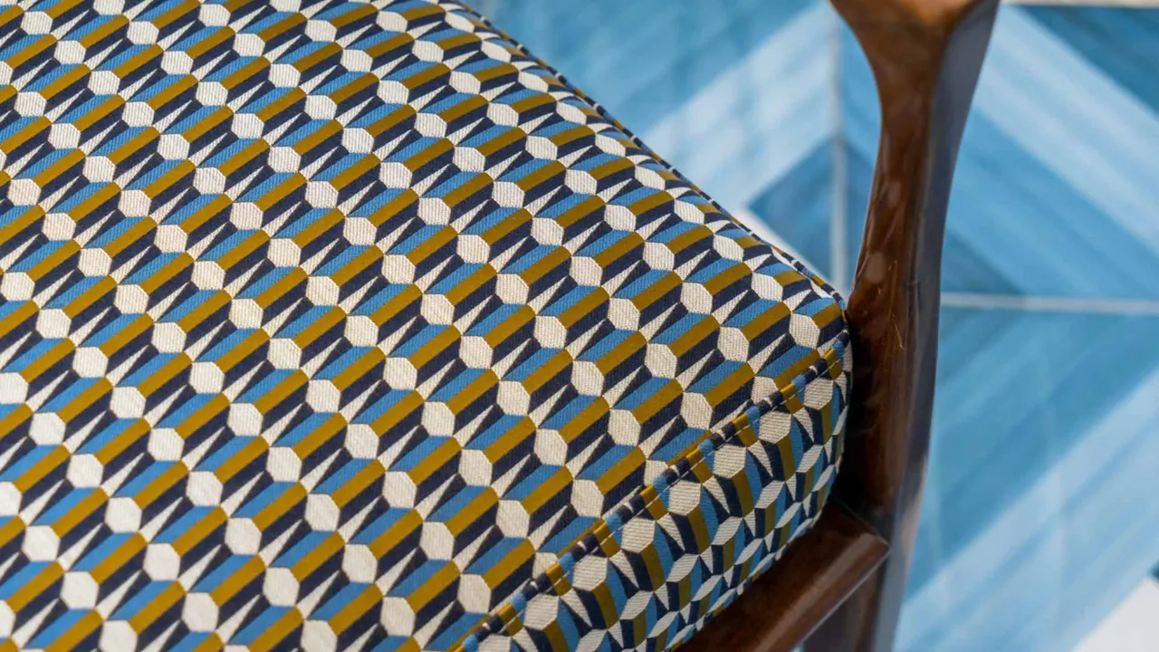 A chair upholstered in a geometric blue and ochre pattern by a window.