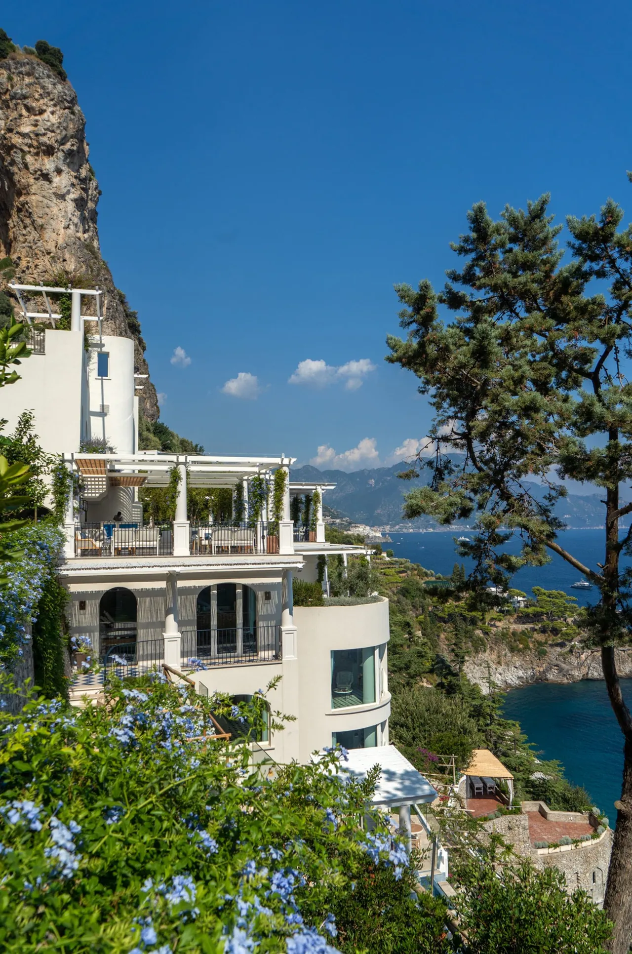 The hotel's terraces stacked on the cliff above the sea, framed by pines.