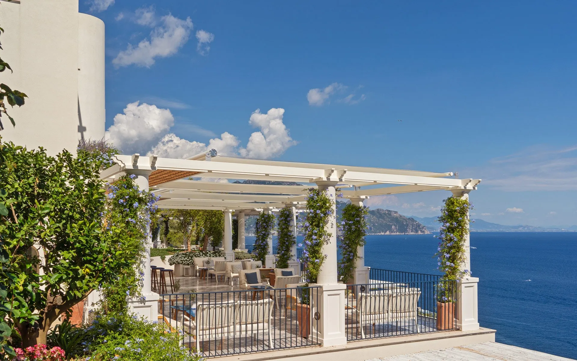 A terrace under a white pergola on the cliff edge, above the open sea.