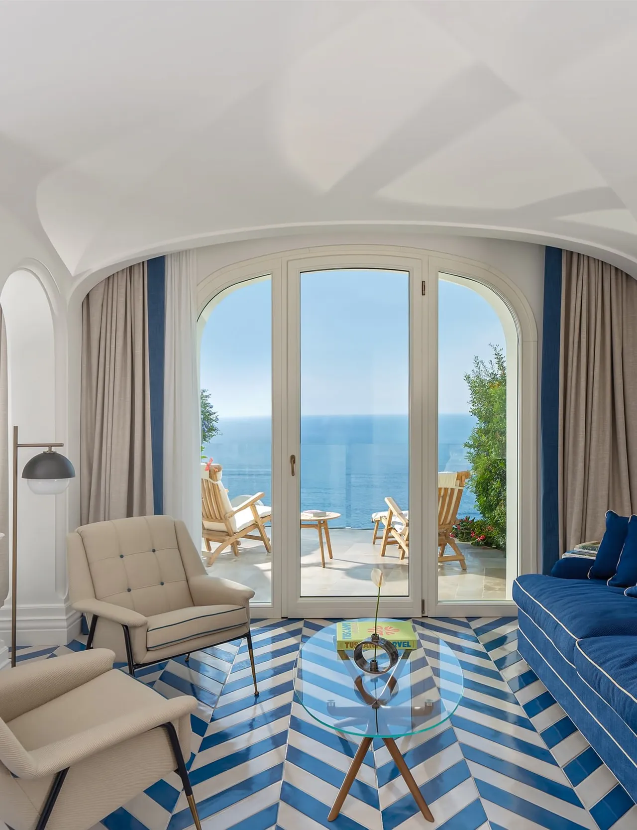 A sitting room with zigzag tiles and arched doors open to a balcony over the sea.