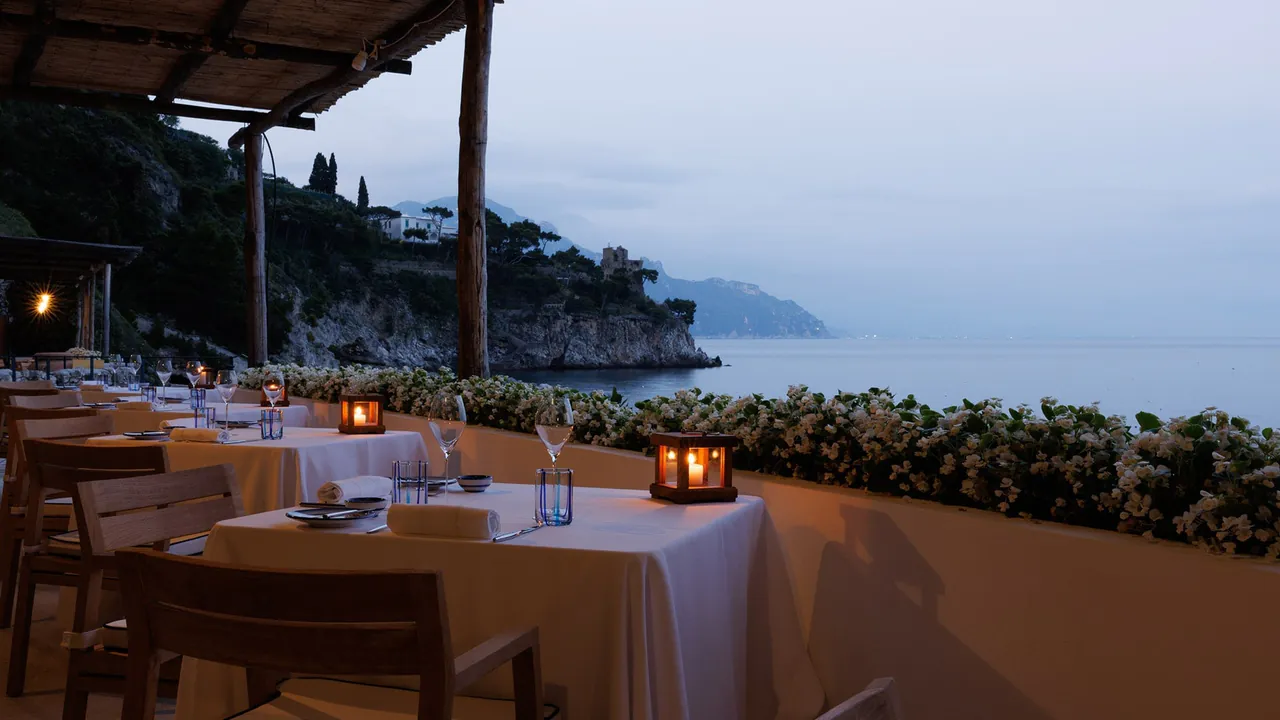 Candlelit tables on a seaside terrace at dusk, with the coast beyond.