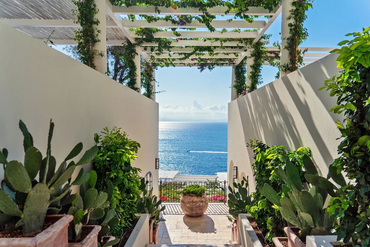 A pergola path between white walls and cacti leads to a view of the sea.