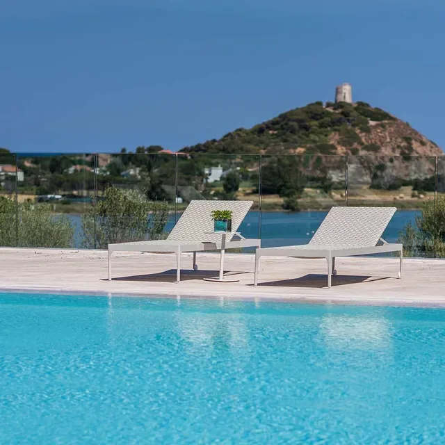 Two white loungers beside a pool at Chia Laguna Resort, Sardinia, facing a lagoon and a hilltop watchtower