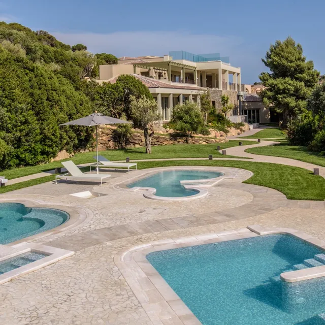 Freeform pools and stone paving at Chia Laguna Resort, Sardinia, below a villa set among green trees