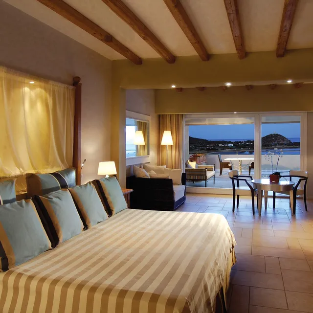 Room at Chia Laguna Resort, Sardinia, at dusk with a striped bed and a terrace facing the coast