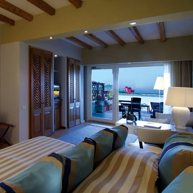 Guest room at Chia Laguna Resort, Sardinia, with striped bedding, beamed ceiling and a sea-view terrace
