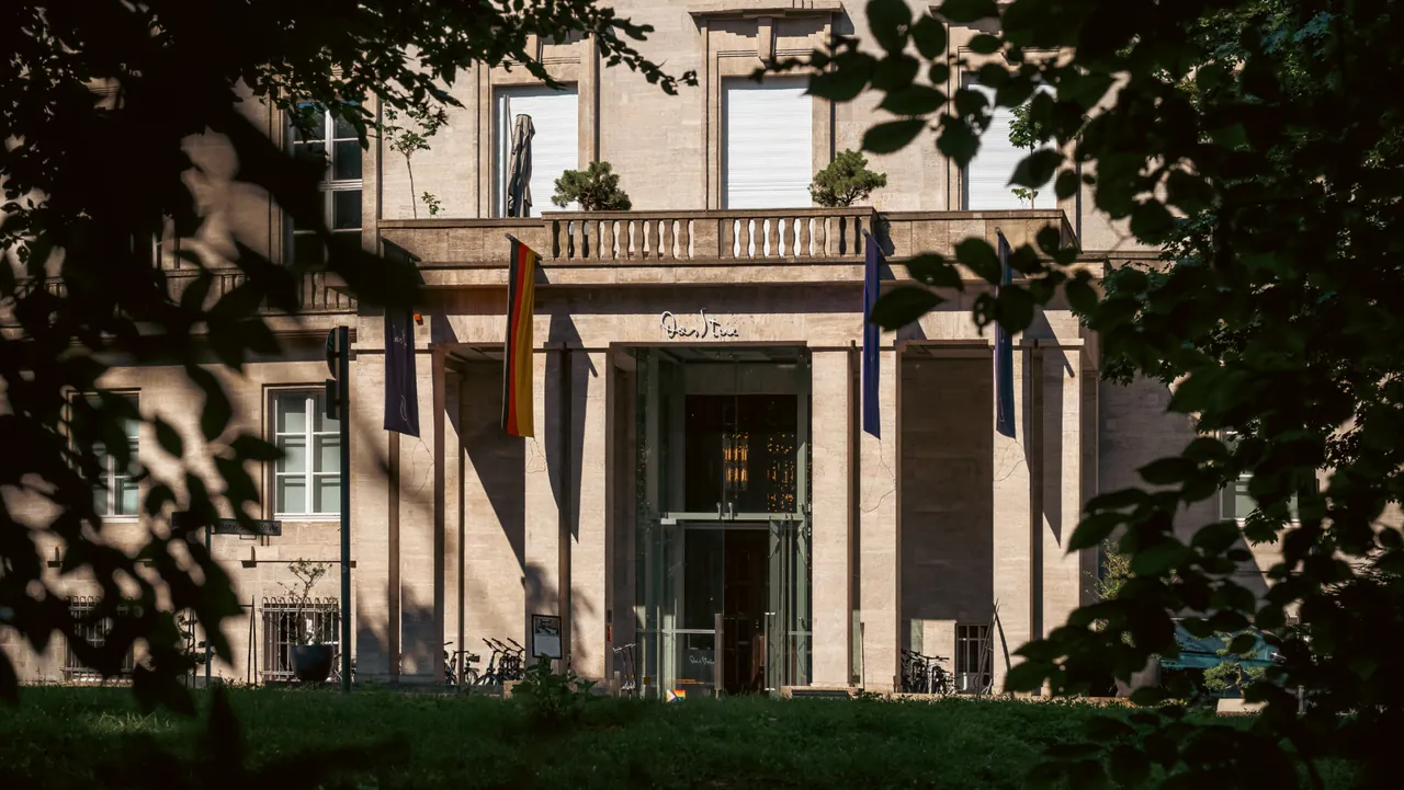 The neoclassical facade of Das Stue framed by trees on the edge of the Tiergarten.