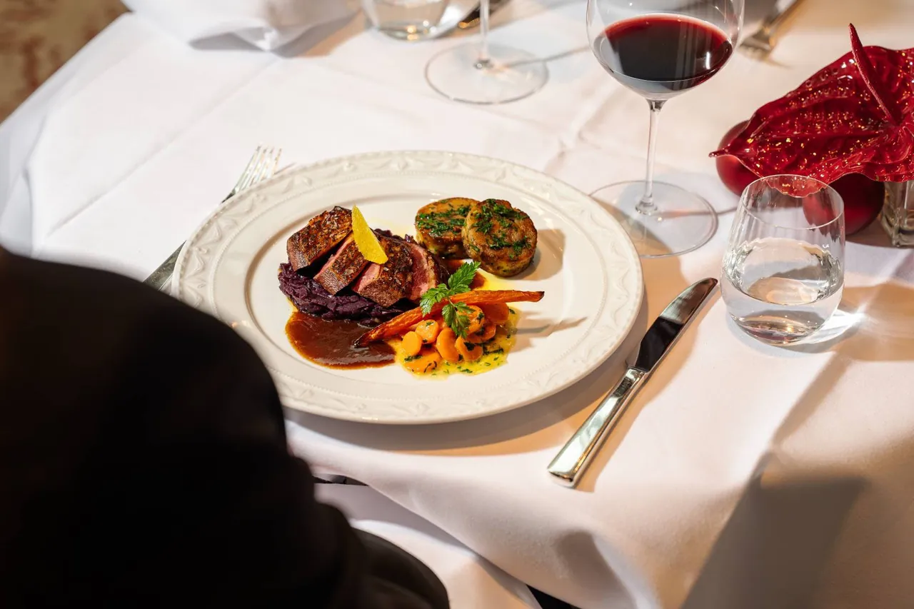 A plated meat dish served with red wine on a white tablecloth.