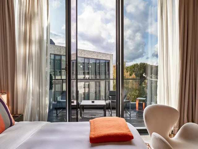 A room with an open balcony door looking out over green treetops.