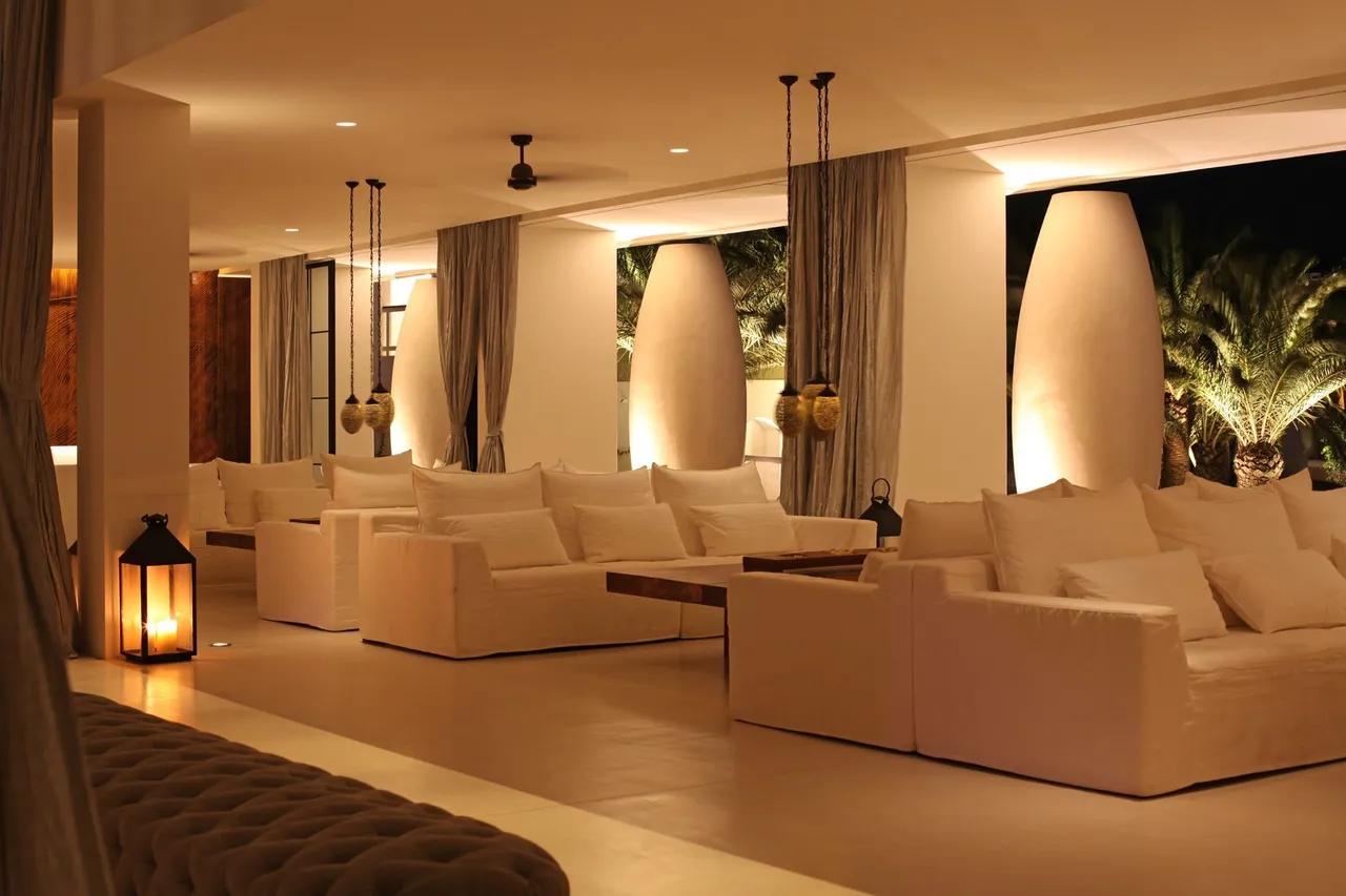 Lounge at Destino Five Ibiza at night with white sofas, lanterns, tall white urns and lit palm trees