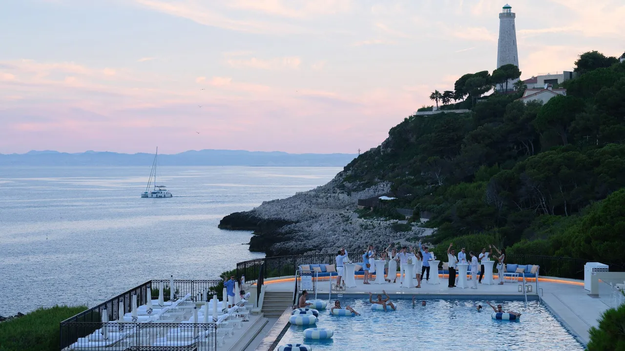 The Club Dauphin pool at dusk, with the Cap-Ferrat lighthouse on the hill above.
