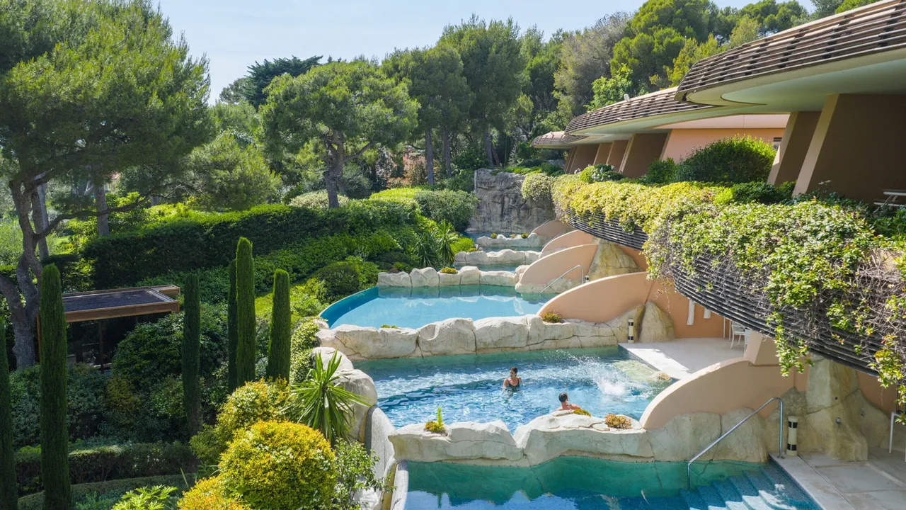 Terraced pools below the curved suites of Les Terrasses du Cap, framed by cypresses.