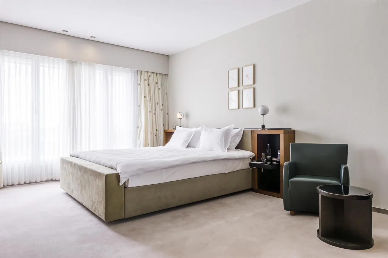 Bright guest room with a large bed, an armchair and sheer curtains.