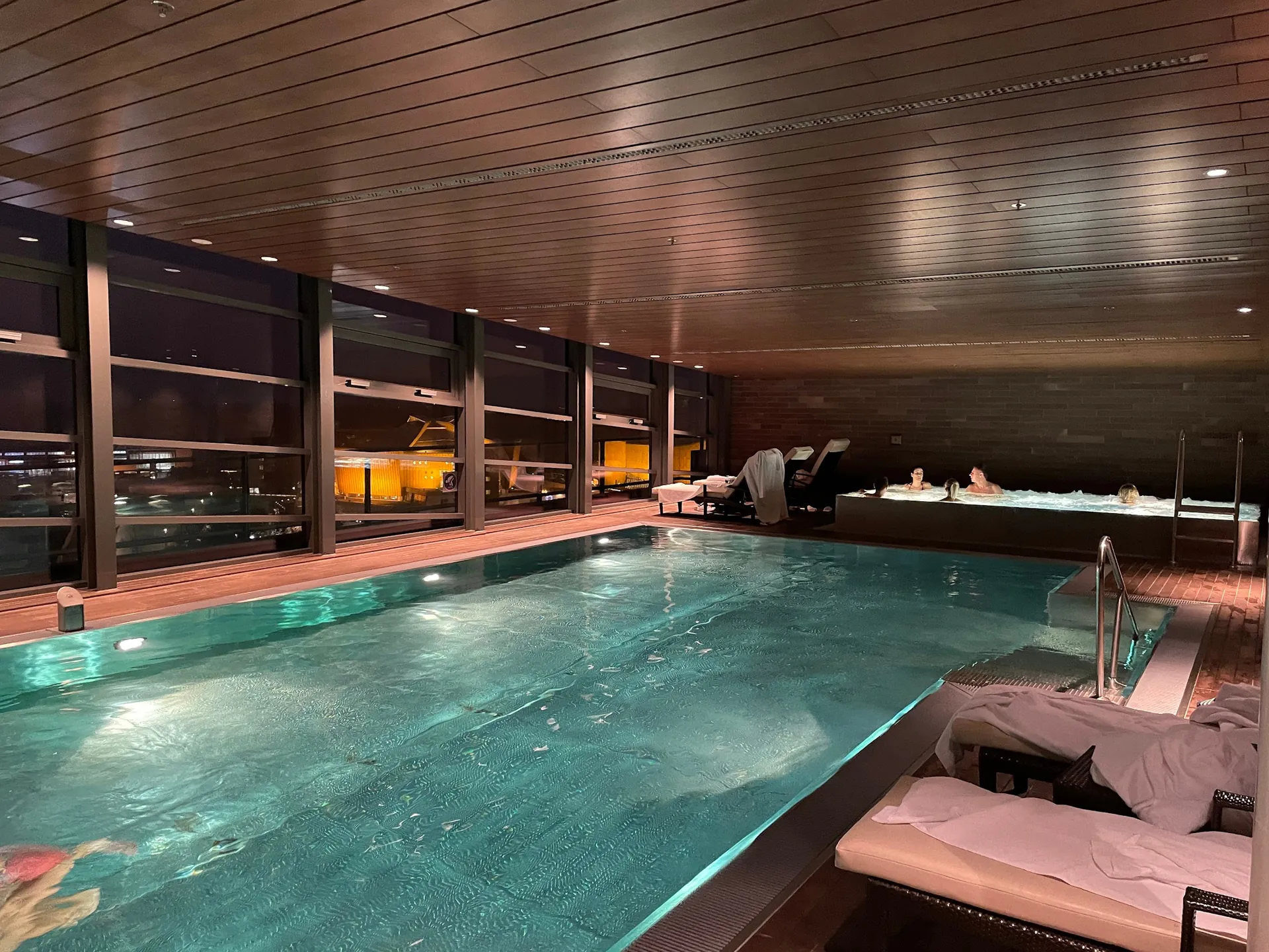 Indoor pool under a wooden ceiling with loungers and a whirlpool.