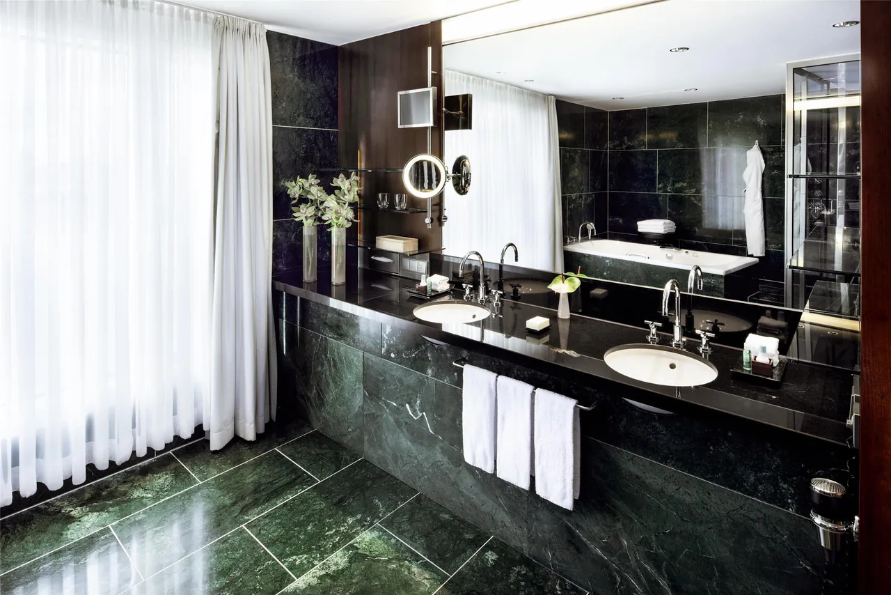 Dark stone bathroom with a long vanity, mirrors and fresh towels.
