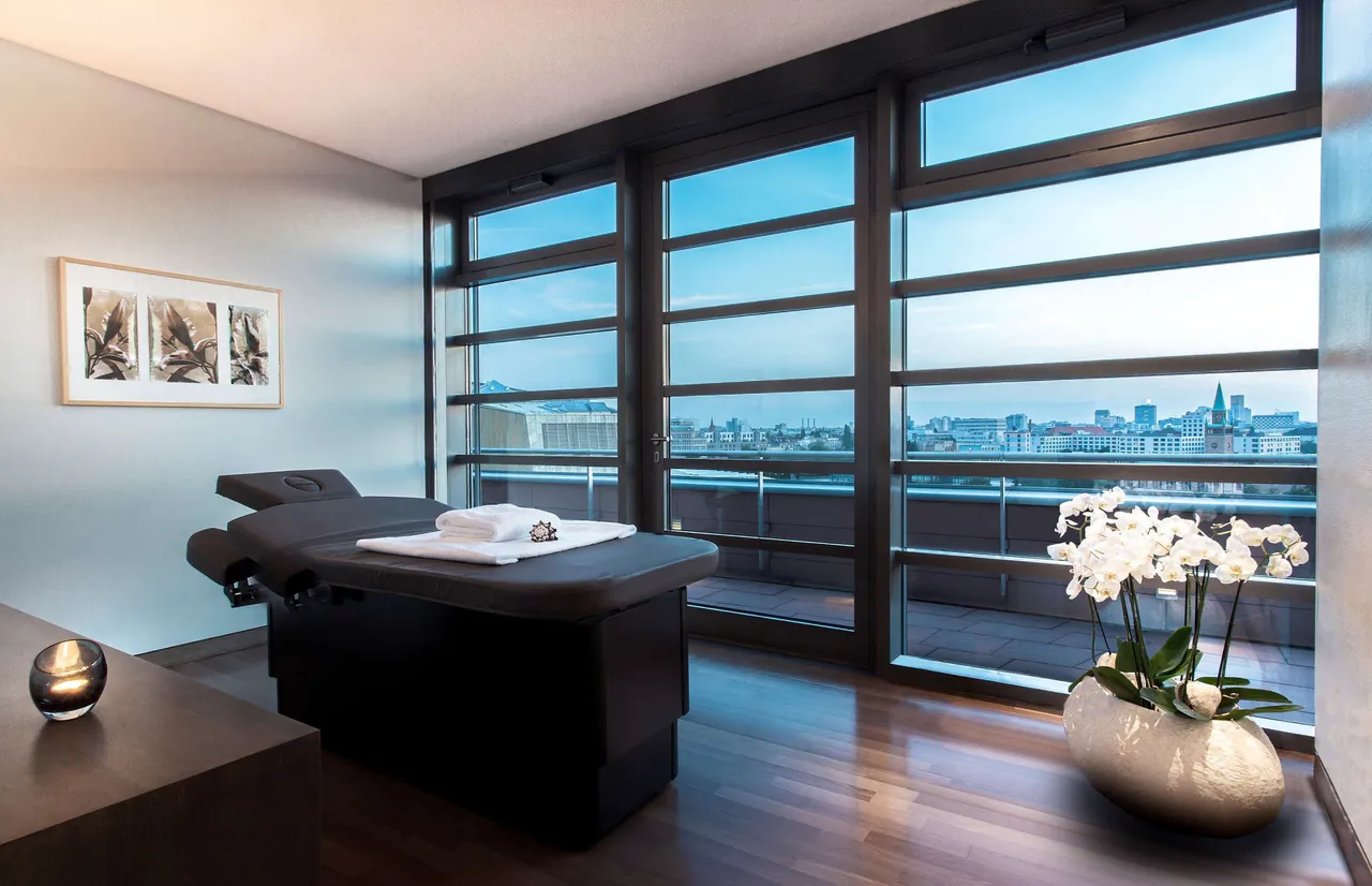 Spa treatment room with a massage bed and wide city views.