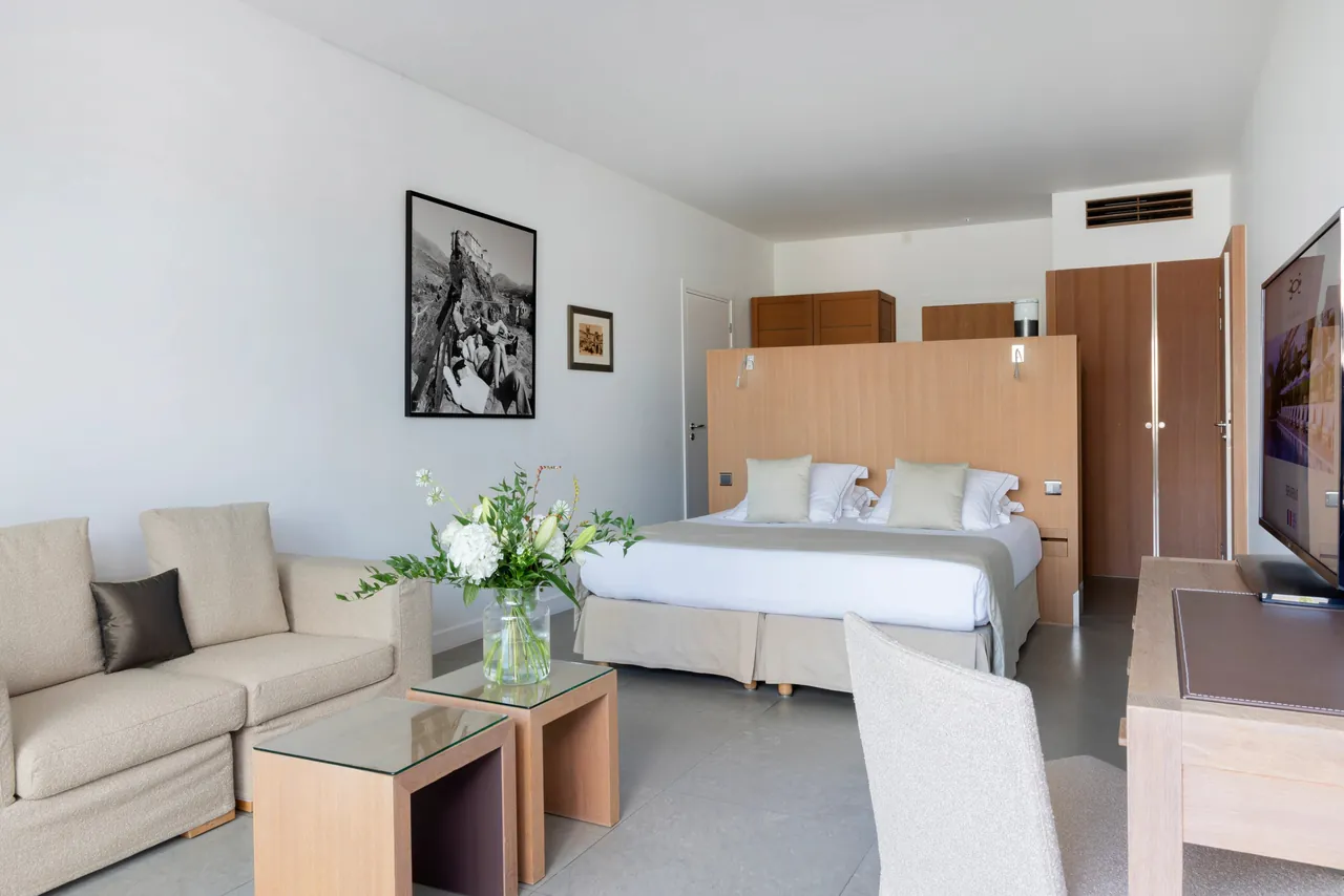 A spacious room with a sofa, a large bed and pale wood panelling.