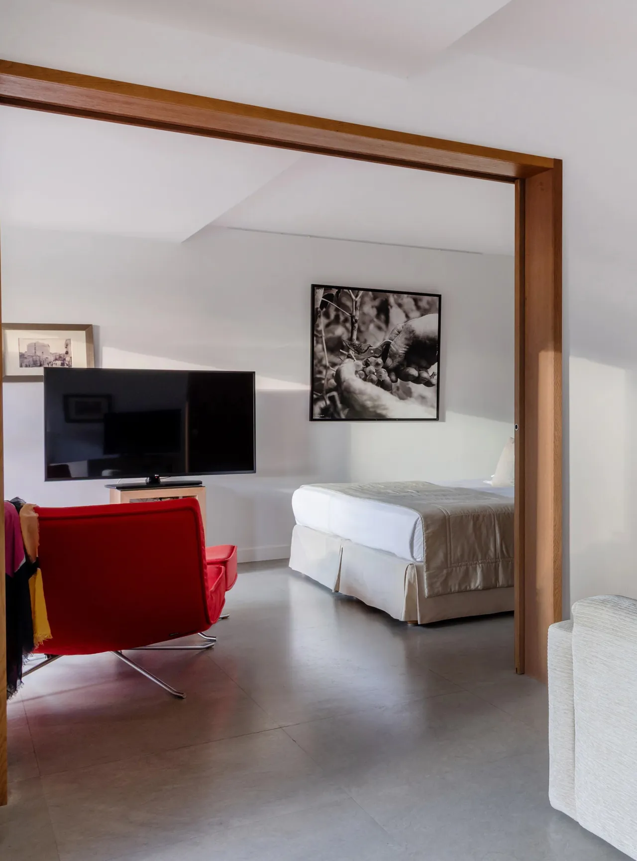 A suite with white walls and a red armchair, the living area opening onto the bedroom.