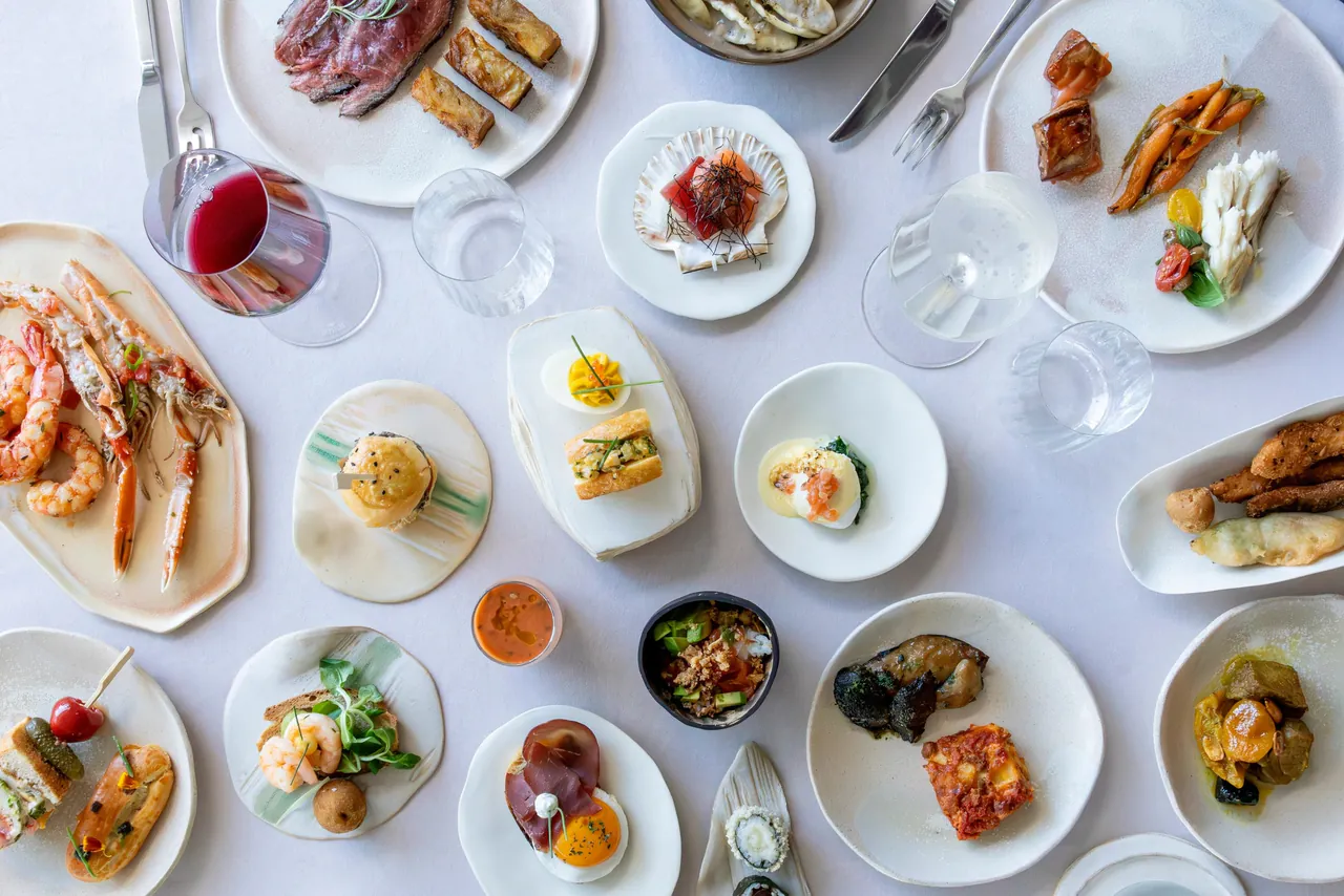 A table seen from above with plates of seafood, salads, bread and red wine.