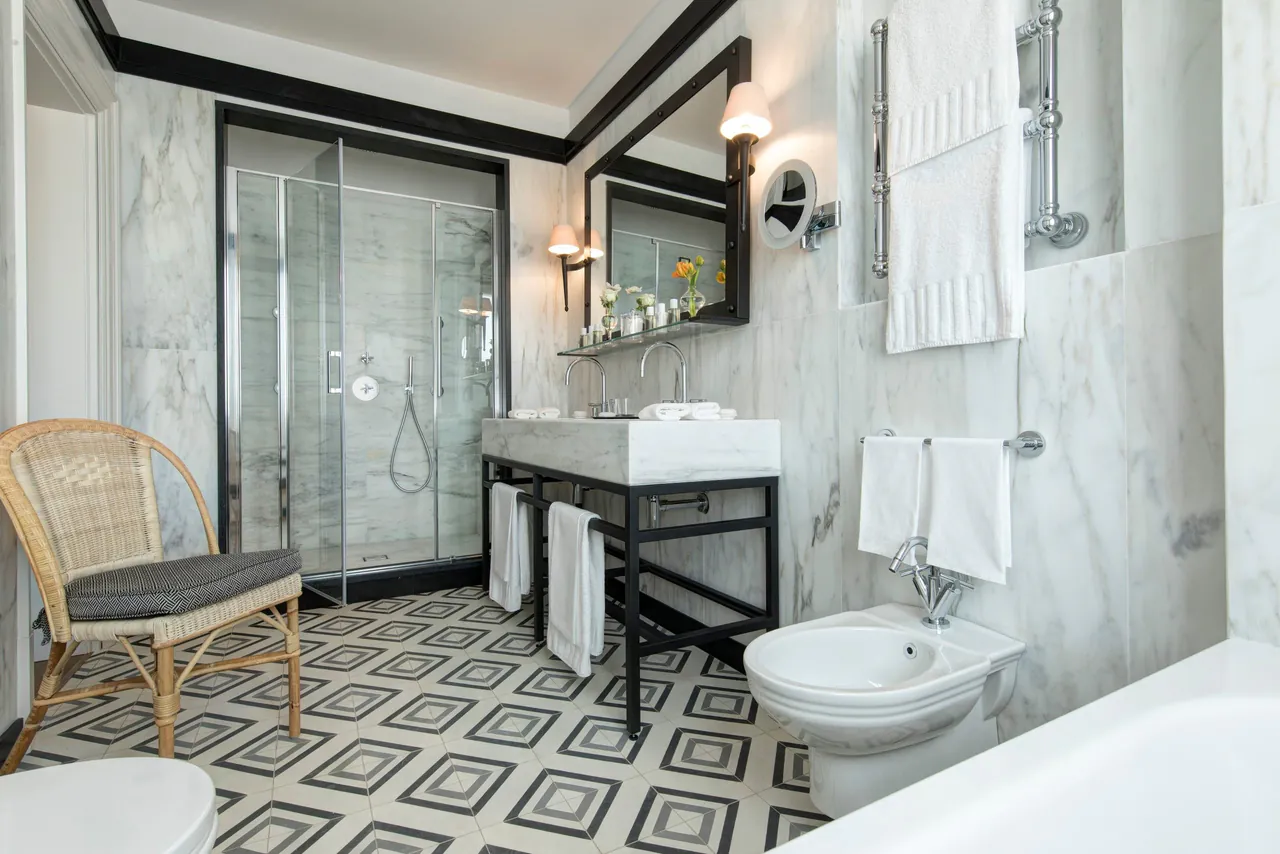 A marble bathroom with a glass shower and a patterned tiled floor.