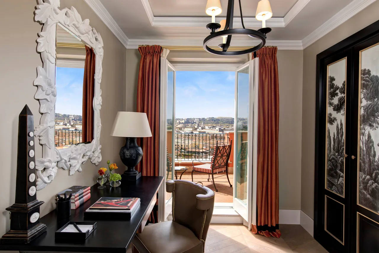 A suite desk beside open doors leading to a terrace with city views.