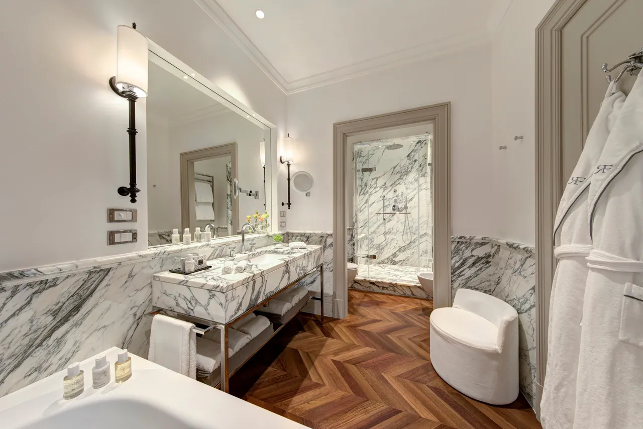 A marble bathroom with double basins and a herringbone wooden floor.