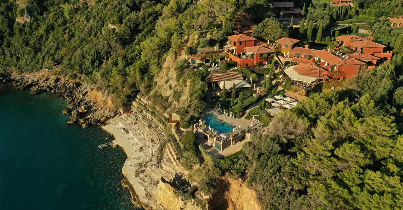 Aerial view of the hotel's terracotta villas spread across a wooded cliff above the sea.
