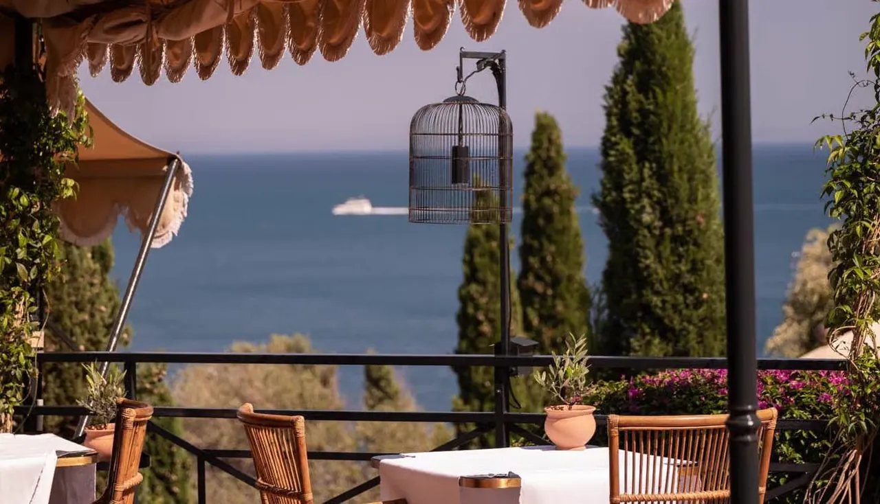 The restaurant terrace with cypress trees and a view over the bay.