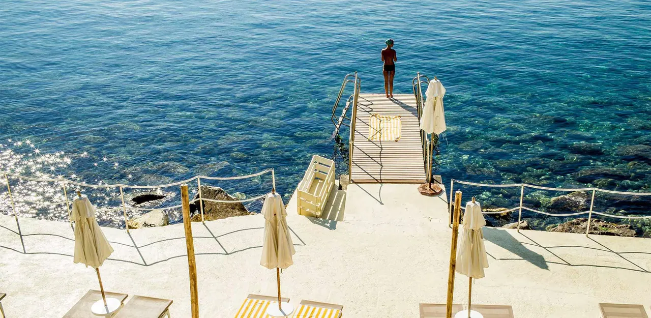 A guest standing at the end of the stone jetty over clear blue water.