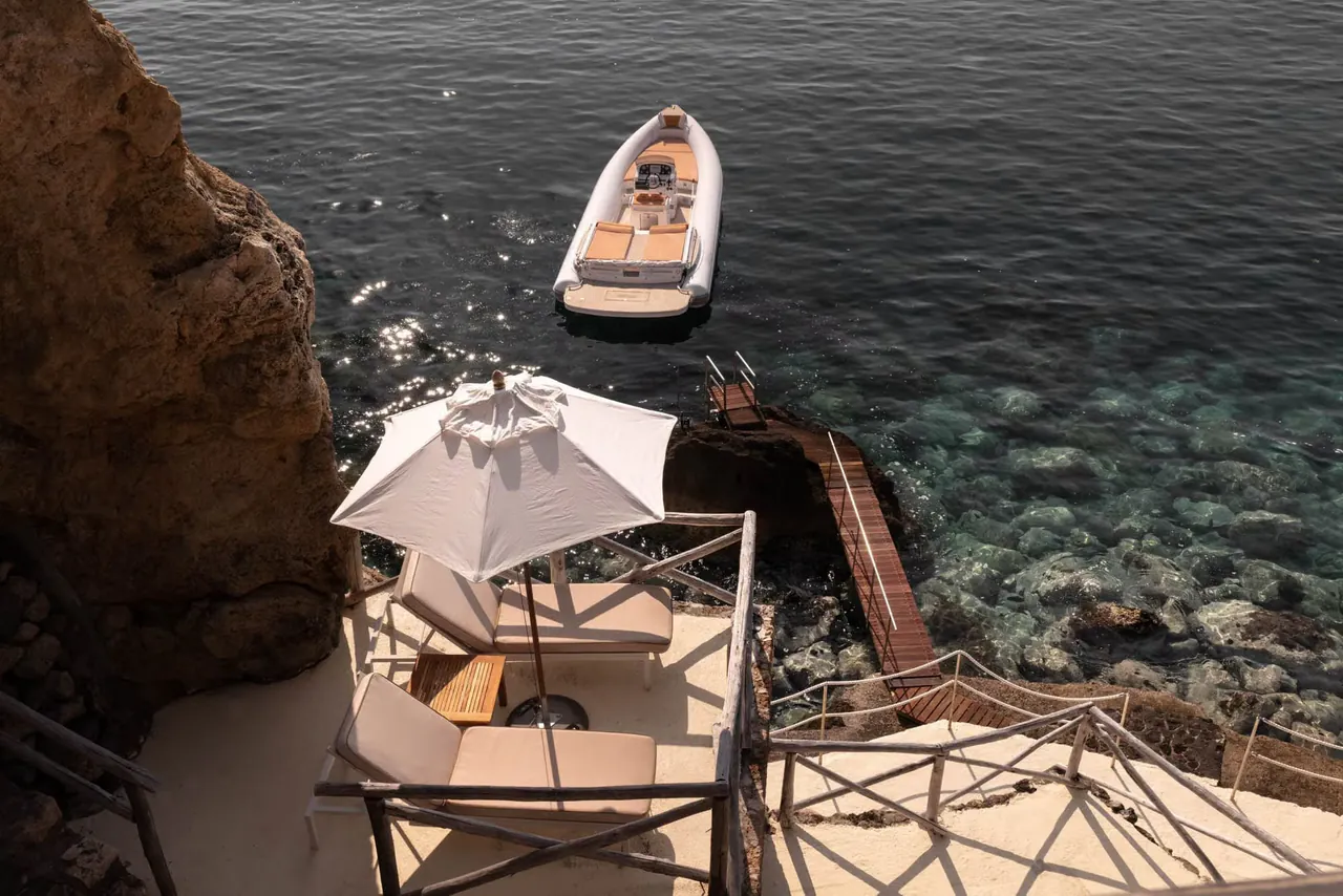 A small motorboat moored beside the sea deck at the foot of the cliff.