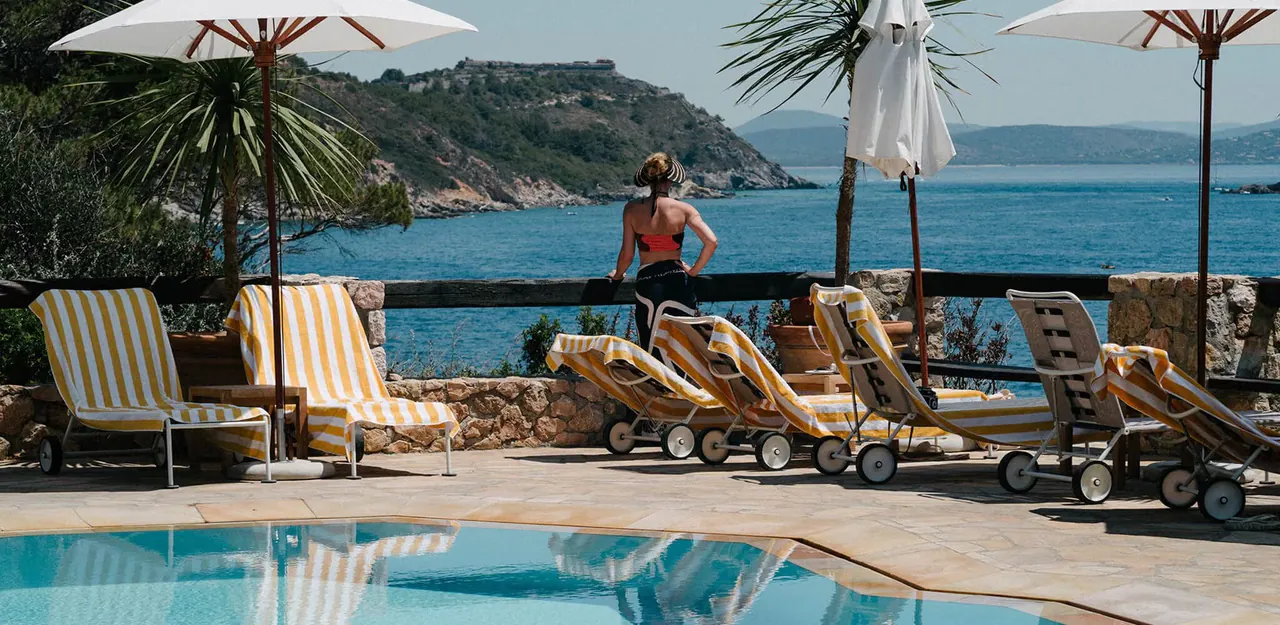 Sun loungers and parasols beside the pool with the bay beyond.