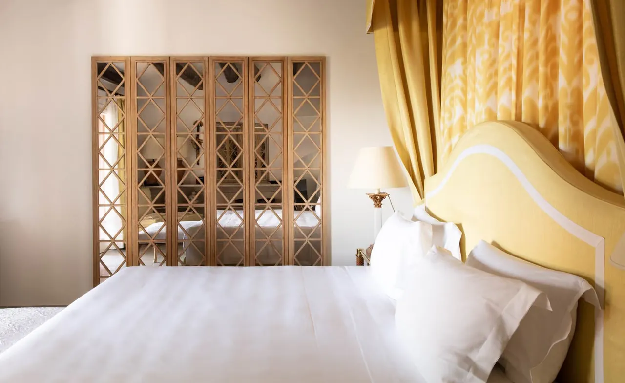 A bright suite bedroom with a yellow headboard and patterned wooden screens.
